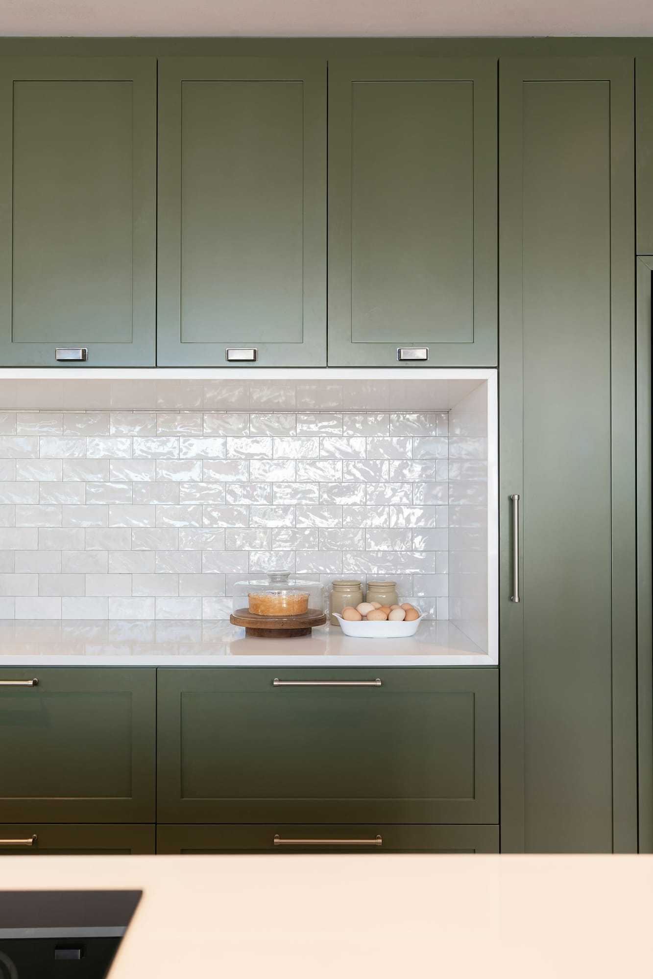 Green kitchen units with a tiled recess
